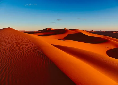 The vast and breathtaking dunes of the Sahara Desert in Morocco, captured at sunset with a silhouette of a camel caravan.